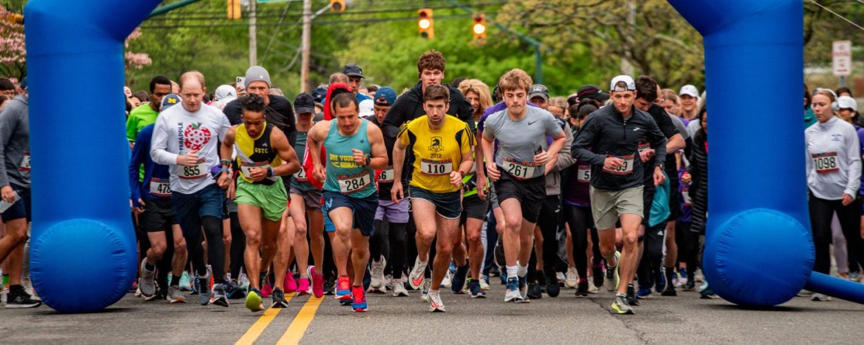 A group of people excitedly running through an obstacle course at the Mothers Day 5k Starting line dash